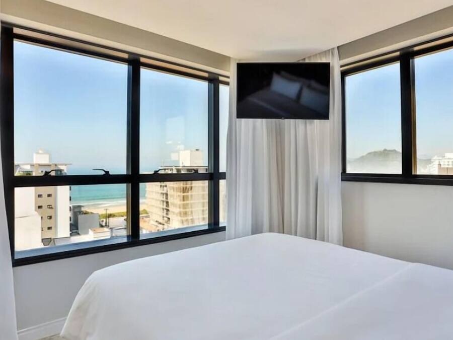 A hotel room with a bed, large windows, and a TV on the wall.