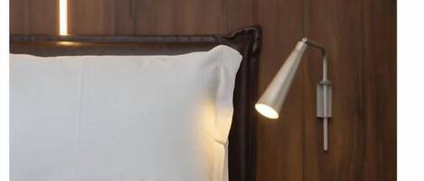 A bed with white bedding, a wooden headboard, and a wall-mounted nightstand with a lamp.
