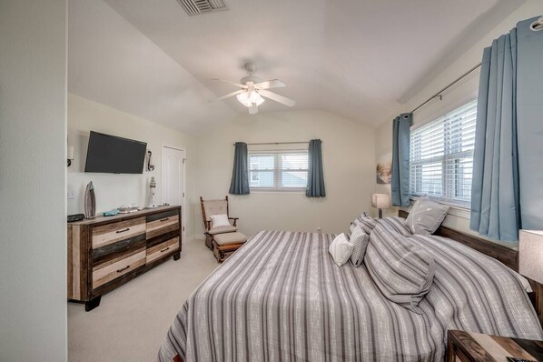 A bedroom with a bed, dresser, chair, and a ceiling fan.