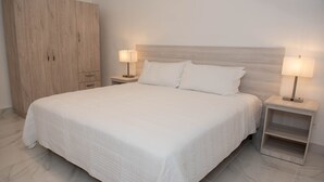 A neatly made bed with a wooden headboard, two bedside tables with lamps, and a large wardrobe. - Casa Bianca (Panama City)