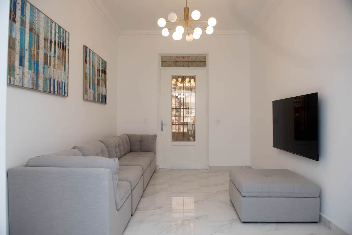 A modern living room with a sectional sofa, a small ottoman, a flat-screen TV, and abstract art on the walls.