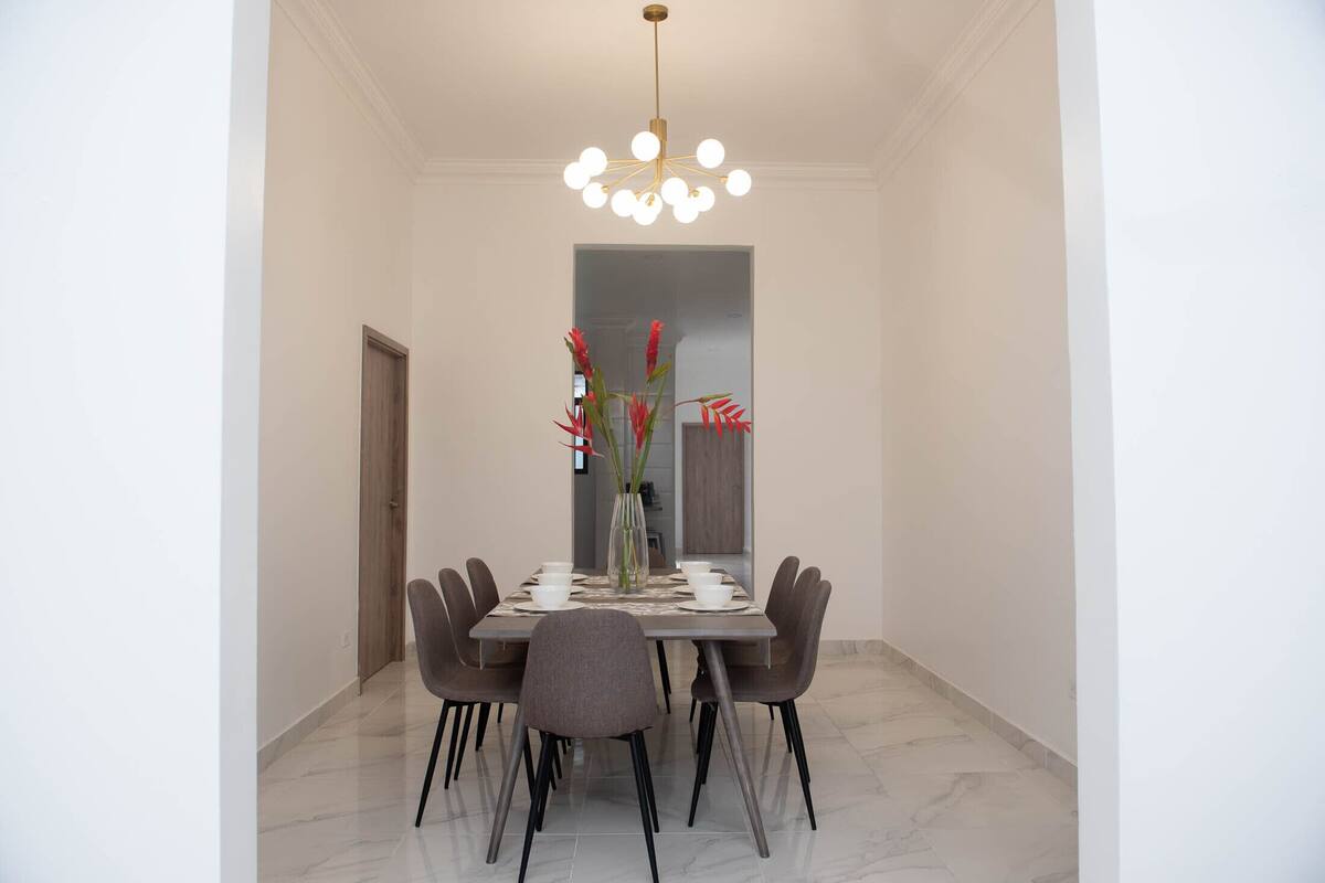 A dining area with a marble floor, a modern chandelier, and a vase with red flowers on the table.