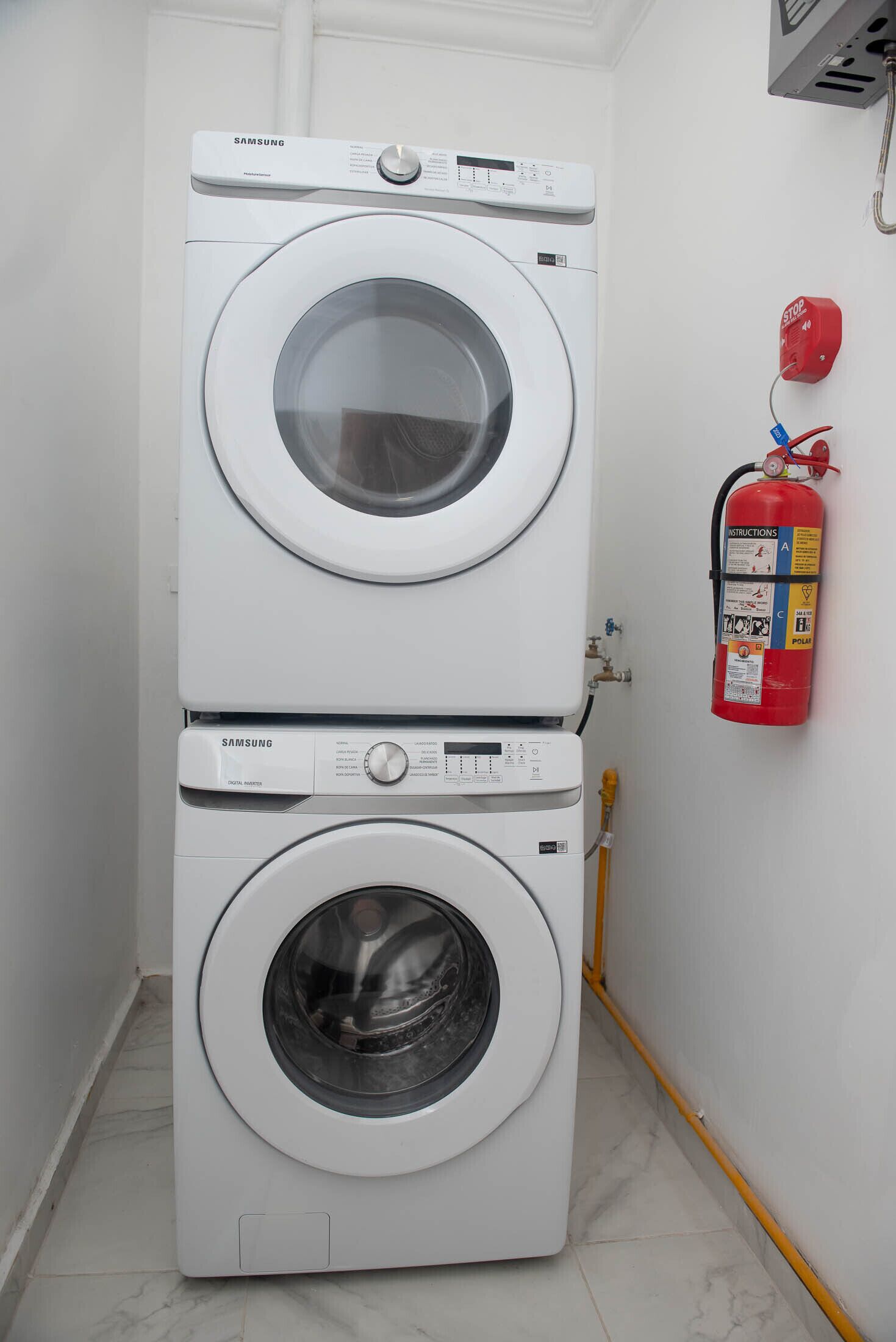 A stacked washer and dryer unit in a laundry room with a fire extinguisher mounted on the wall.