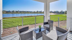 A covered outdoor area with wicker furniture and a view of a lake and distant houses.