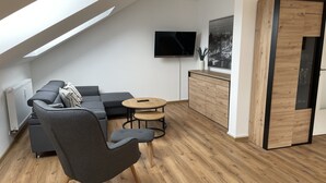 Moderni olohuone, jossa on kulmasohva, pyöreä sohvapöytä ja seinälle asennettu televisio.