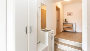 Passadís amb un armari blanc, un mirall, un petit lavabo amb un ram i una estant amb cistelles.