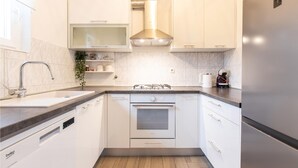 Una cuina moderna amb armaris blancs, una campana extractora d'acer inoxidable, forn integrat i nevera.
