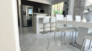 A modern kitchen with a stainless steel refrigerator, a microwave, and a large island with bar stools. - JC’s Modern Paradise (Chula Vista)