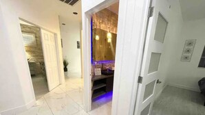 A hallway with a marble floor leading to a room with a wooden door and a blue-lit area. - JC’s Modern Paradise (Chula Vista)