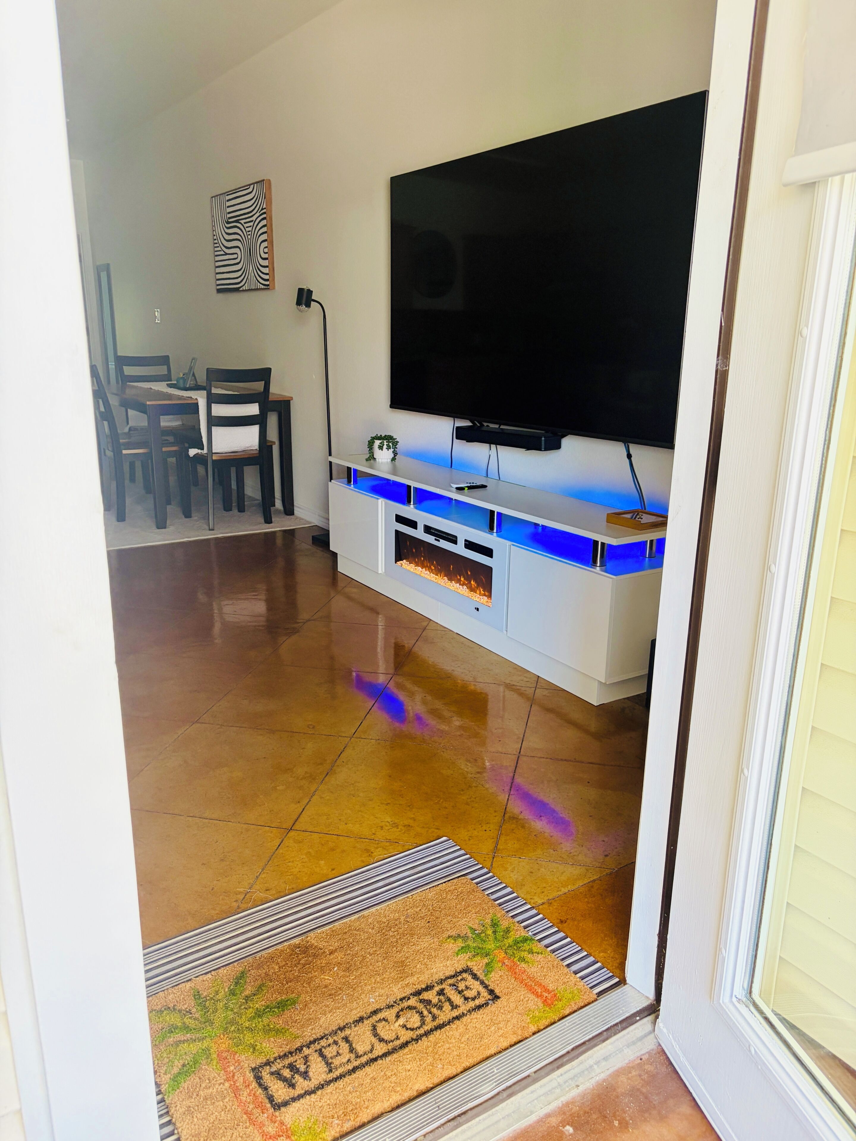 Un salon doté d’un téléviseur à écran plat fixé à un meuble de rangement blanc, d’un coin repas avec des chaises et une table, et d’un plancher en bois poli.