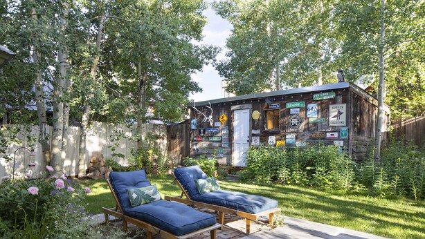 A wooden cabin with a deck, surrounded by lush greenery and trees.