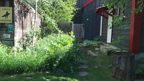 A backyard with a wooden fence, a sign indicating a surfer crossing, and a Pacific Coast Highway sign.