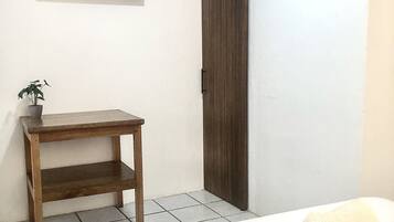 Un dormitorio con cama, mesita de noche de madera, planta en maceta, televisor montado en la pared y puerta corredera.