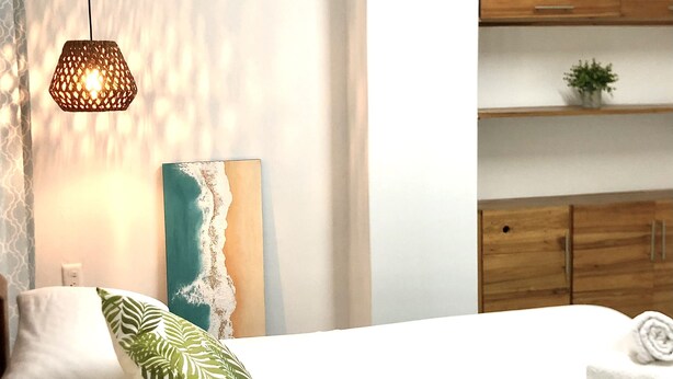A modern bedroom with a bed, a hanging light fixture, wooden cabinets, and a wall art piece. - Hotel playas (Pedernales)