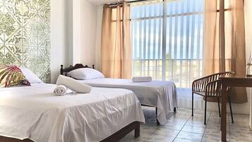 Una habitación de hotel con dos camas, una silla de madera y un ventanal con cortinas.