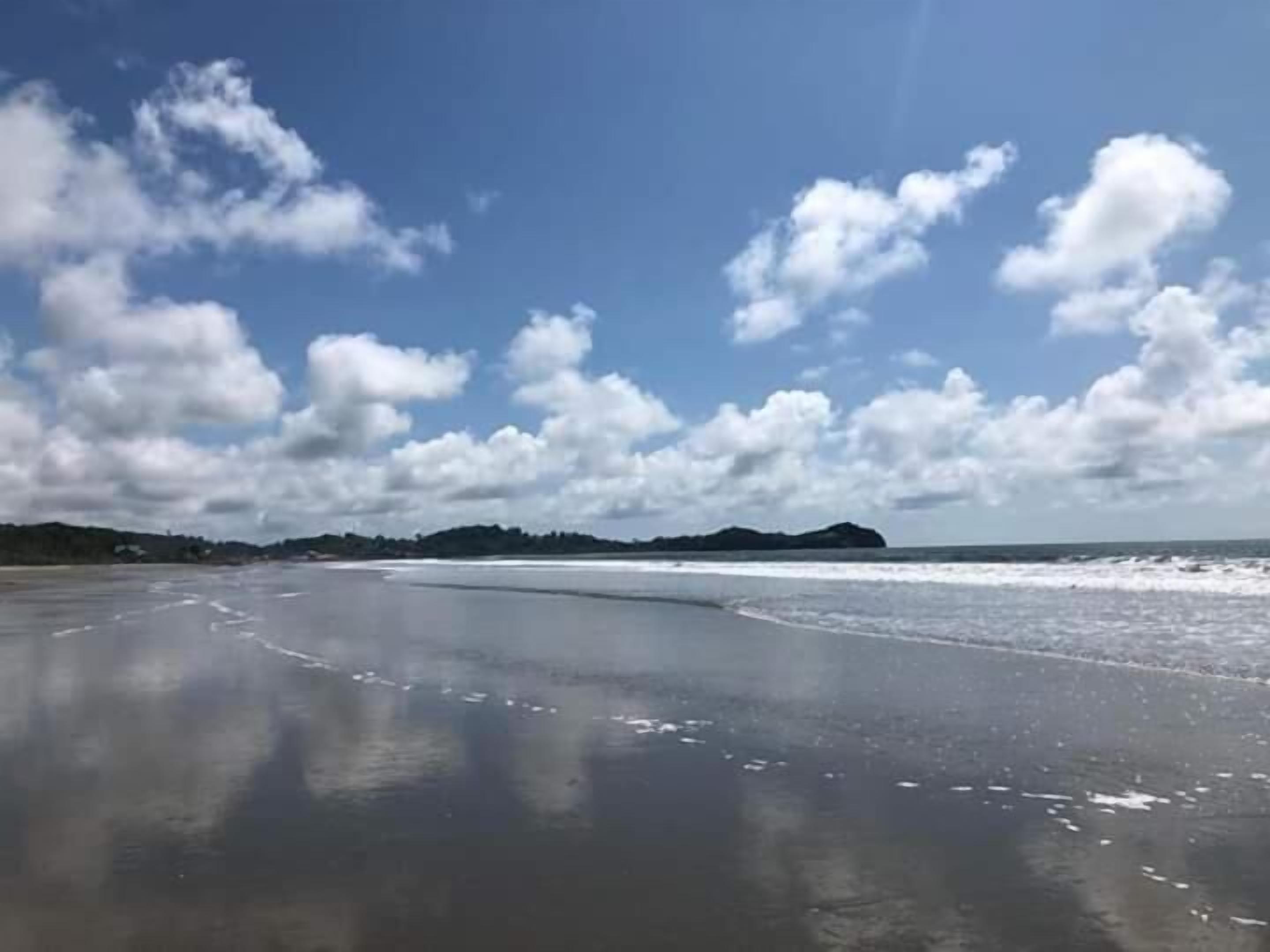A beach with a wide sandy shore, calm water, and a distant island.
