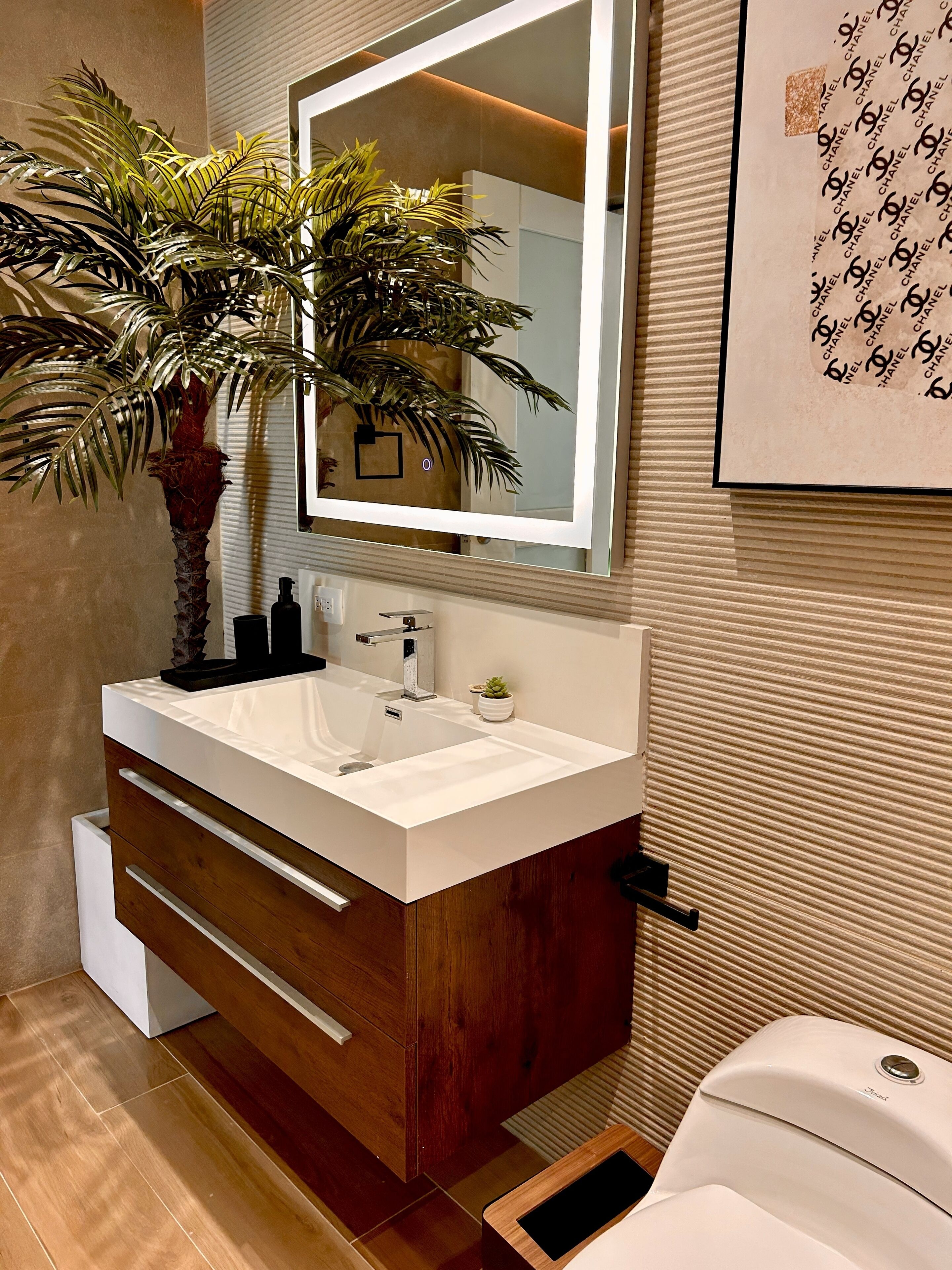 Un baño moderno con un lavabo blanco, tocador de madera, un espejo grande y una planta en maceta.