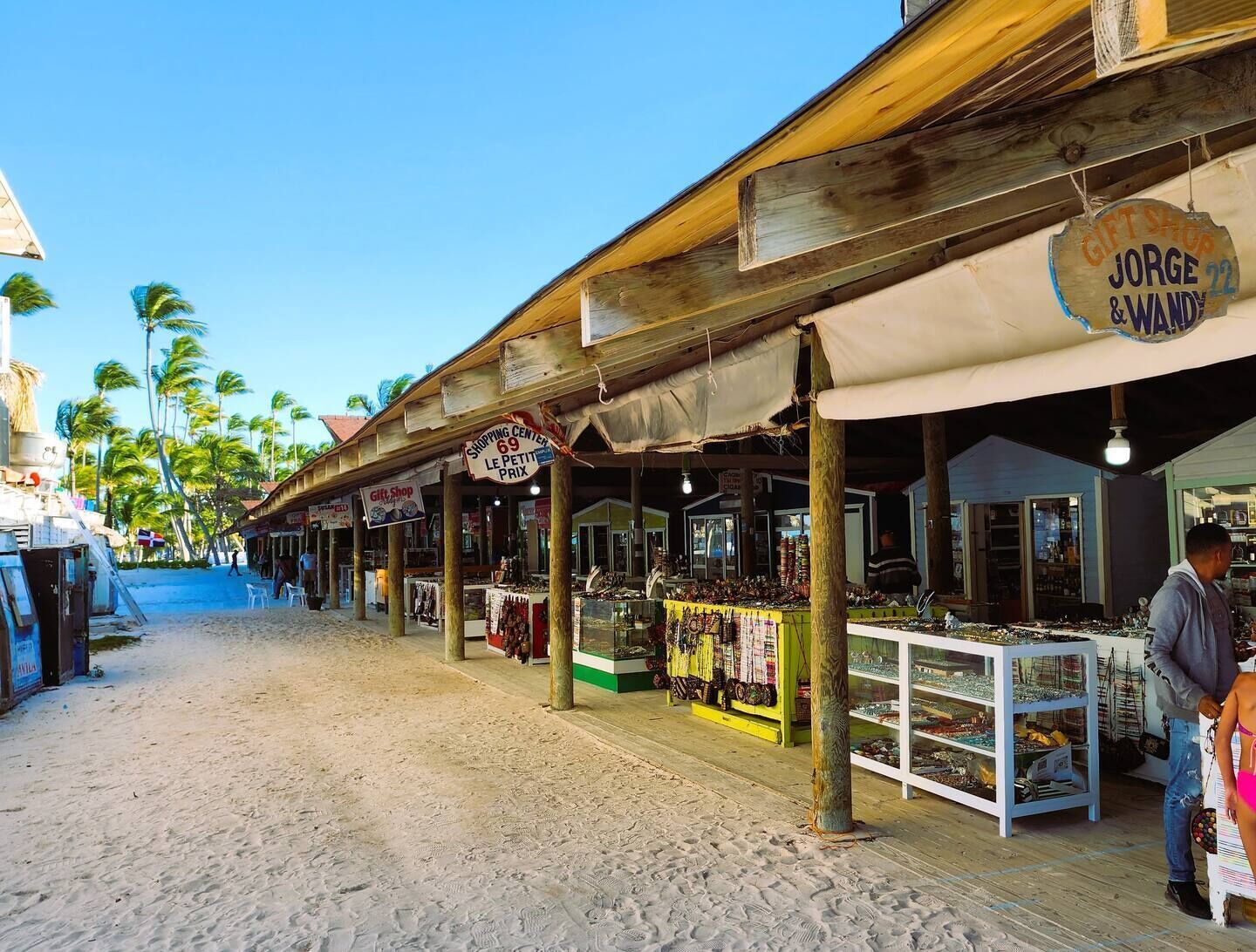 Un marché installé au bord de la plage, avec des étals en bois et une enseigne indiquant « Jorge et Wanda ».