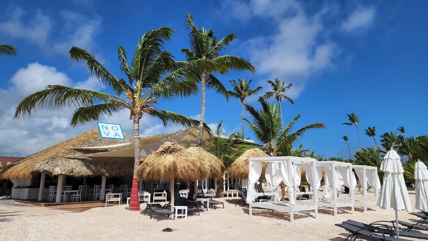 En restaurant ved stranden med stråtage, hvide parasoller og liggestole.