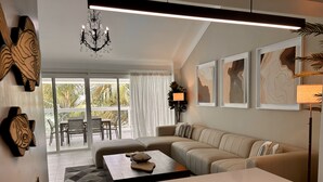 Un salon moderne avec un grand canapé d’angle, une table basse et un coin repas comprenant une table et des chaises. On peut y admirer des tableaux abstraits encadrés accrochés au mur, un lustre et un lampadaire.