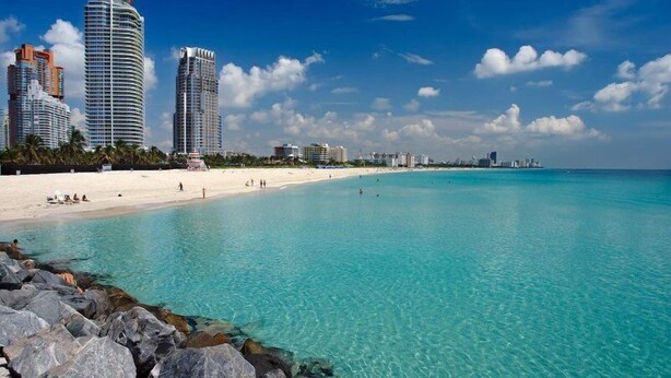 A beach with clear turquoise waters, a sandy shore, and modern high-rise buildings in the background. - Royal Hotel Unit 337 (Miami Beach)