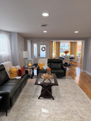 A living room with a leather sofa, a glass coffee table, and a dining area with a table and chairs. - Colonial Oasis of Peace 5 Guest (Utica)