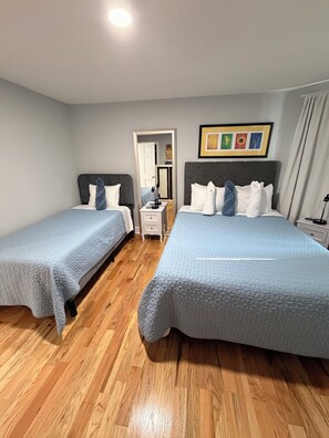 A hotel room with two beds, wooden flooring, a small bedside table, a mirror, and a framed picture on the wall. - Colonial Oasis of Peace 5 Guest (Utica)