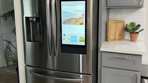 Ruostumattomasta teräksestä valmistettu Samsung-jääkaappi, jossa on digitaalinen näyttö, harmaat ovet ja työtasolla puinen leikkuulauta.