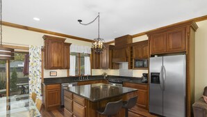 A kitchen with wooden cabinets, a stainless steel refrigerator, a microwave, and a granite countertop island with bar stools. - Condo in the Heart of Douglas - Chef's Kitchen (Douglas)