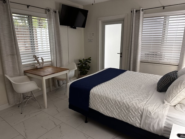 Quarto com cama, escrivaninha, cadeira, televisão e um vaso de planta.