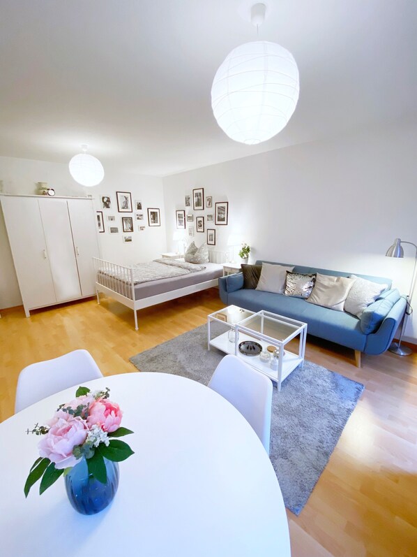 Ett modernt vardagsrum med en vit soffa, ett soffbord och ett matbord med en vas med blommor.