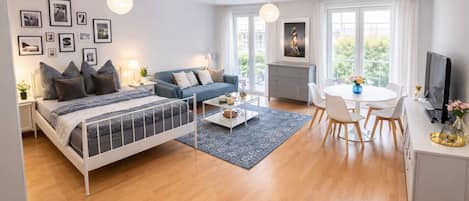 A modern living room with a bed, sofa, coffee table, and dining area.