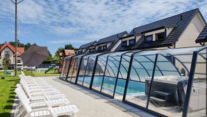 A swimming pool with a glass enclosure, surrounded by white lounge chairs and a covered area.