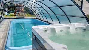 A covered swimming pool with a hot tub, surrounded by a transparent roof structure.
