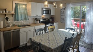 A kitchen with white cabinets, a microwave, and a coffee maker. There is a dining table with chairs and a sign on the wall.
