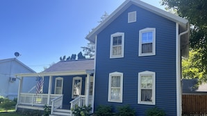 A two-story blue house with a porch, a satellite dish, and a small garden.