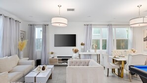 Una sala de estar moderna con sofá, mesa de centro, televisor y zona de comedor con sillas y mesa de billar.