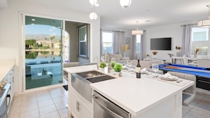Una cocina moderna con una isla central, un comedor con billar y vistas a una piscina y montañas.