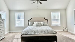 A bedroom with a bed, a ceiling fan, two windows with blinds, a dresser, and a carpeted floor. - Spacious & Cozy Turnkey Master’s Tournament Rental with Concierge Level Service (Grovetown)