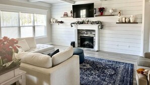A living room with a fireplace, a television mounted above it, and a ceiling fan. - Spacious & Cozy Turnkey Master’s Tournament Rental with Concierge Level Service (Grovetown)