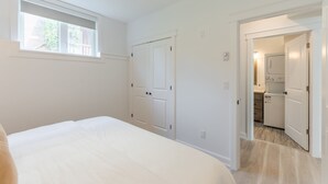 A bedroom with a bed, a window, and a door leading to a laundry room. - Cozy Haven in Port Hope: Explore, Relax, Recharge (Port Hope)