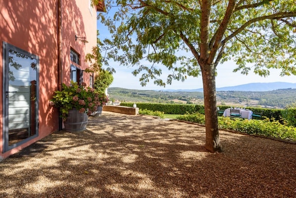 A building with a red exterior, a large tree in the foreground, and a view of rolling hills in the background.