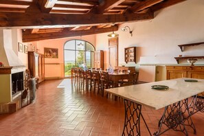 A rustic kitchen with a large dining table, wooden chairs, and a view through a large window.