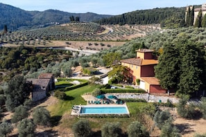 A villa with a swimming pool, surrounded by olive groves and hills.