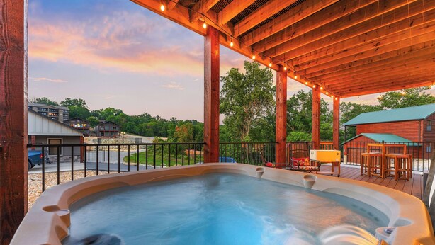 Ein Whirlpool unter einer Holzpergola mit Lichterketten, umgeben von einer Terrasse mit Gartenmöbeln.