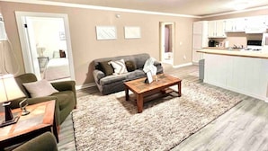 A living room with a grey sofa, a coffee table, and a kitchen area with white cabinets and a countertop. - Pet-Friendly Garrison Cabin (Garrison)