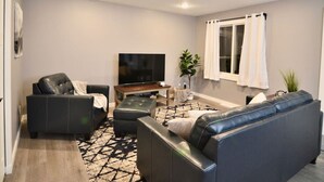A modern living room with a sofa set, a television, and a window with curtains. - Pet-Friendly Garrison Cabin (Garrison)