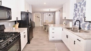A modern kitchen with white cabinetry, a black refrigerator, a stove, and a sink. - Pet-Friendly Garrison Cabin (Garrison)