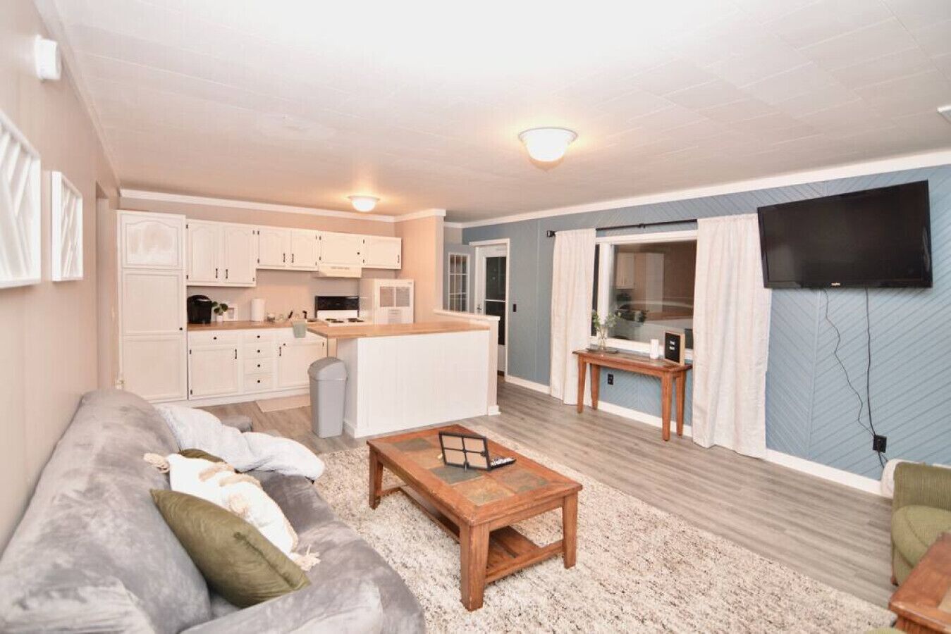Een moderne woonkamer met een grijze bank, een houten salontafel en een keuken met witte kasten.