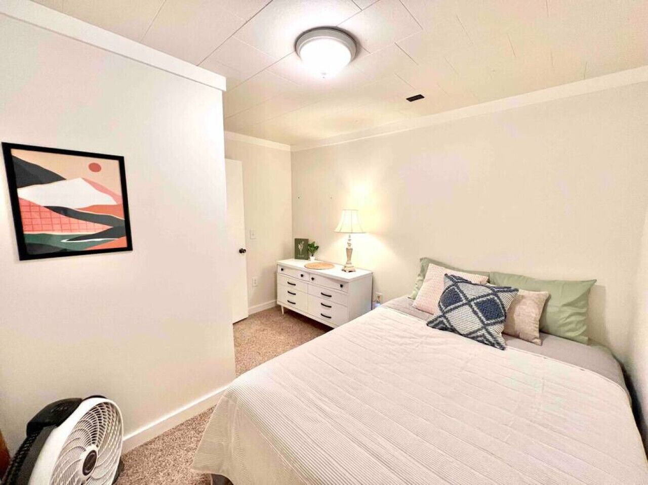 Une chambre à coucher comprenant un lit, une table de chevet, une lampe et une œuvre d’art accrochée au mur.